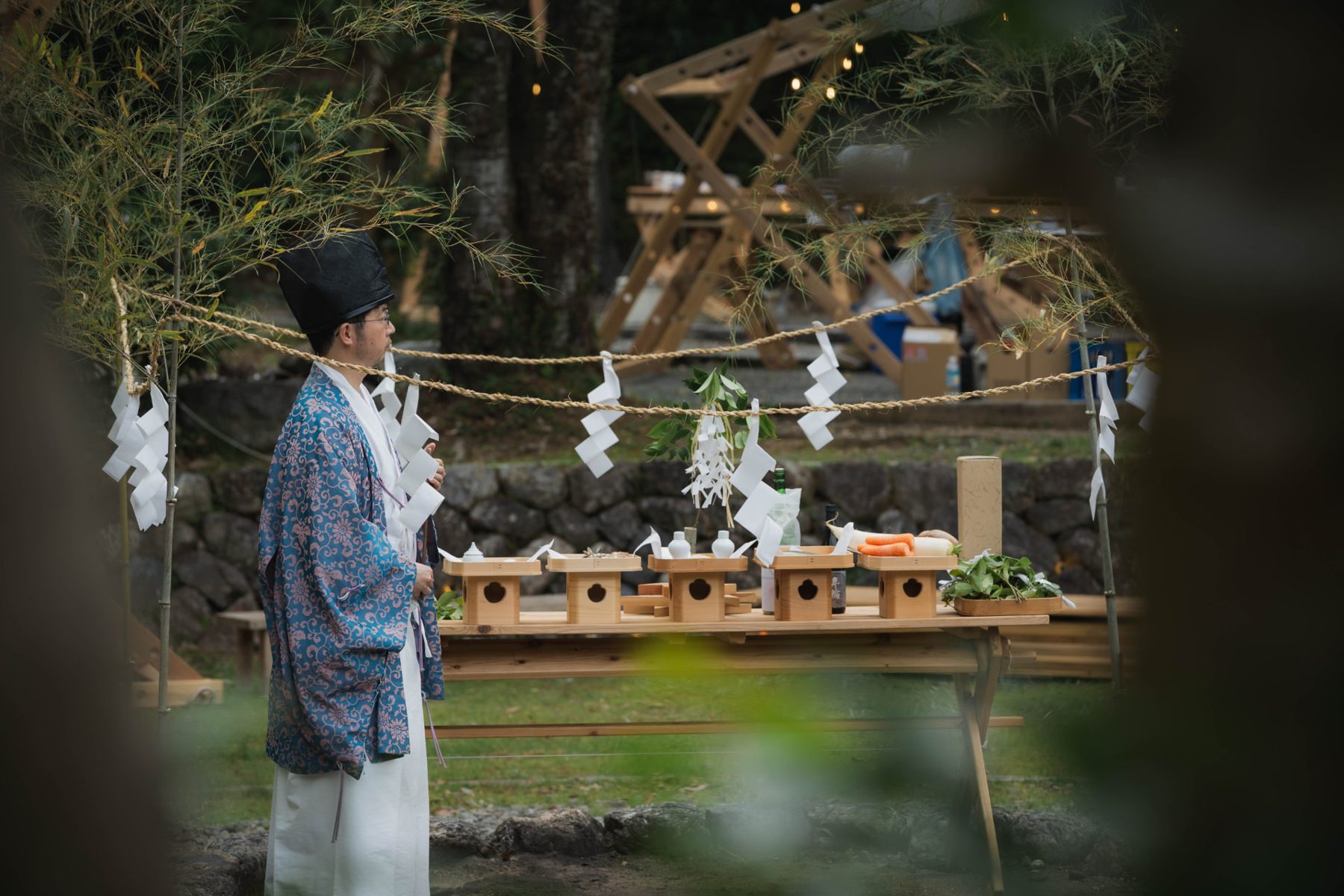 A man in ritual robes beside a wooden altar of food offerings at the opening ceremony