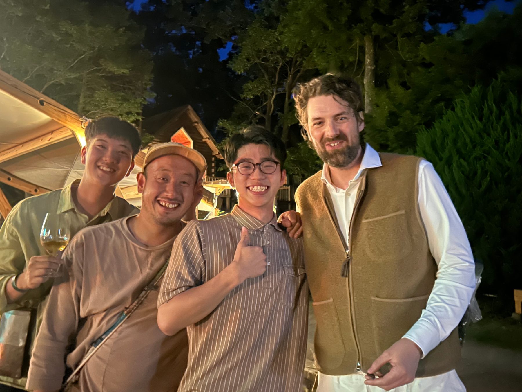 Four guests posing together outdoors at night beside a lit wooden stall