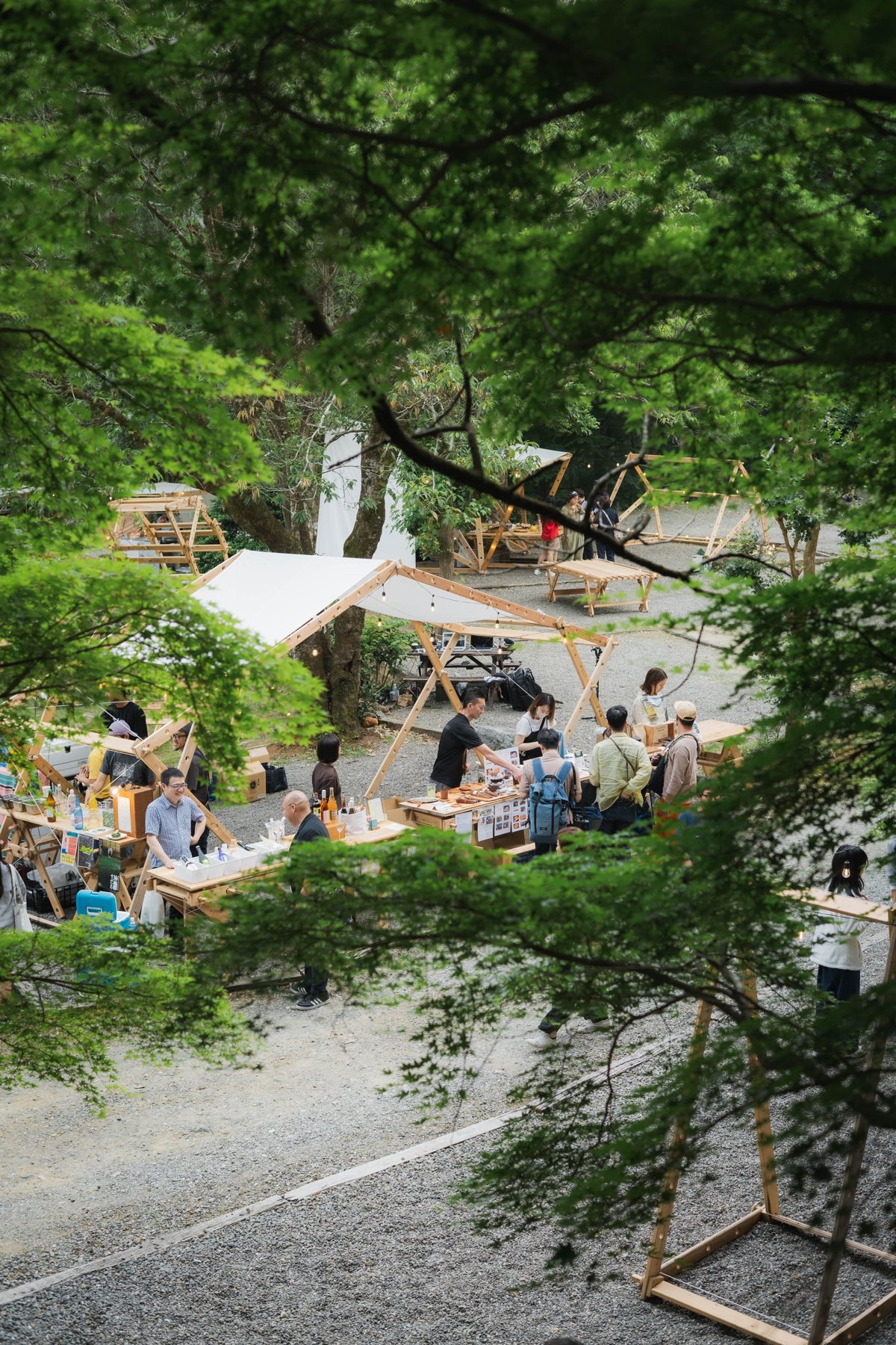 Vendors and visitors at A-frame wooden market stalls in a gravel courtyard