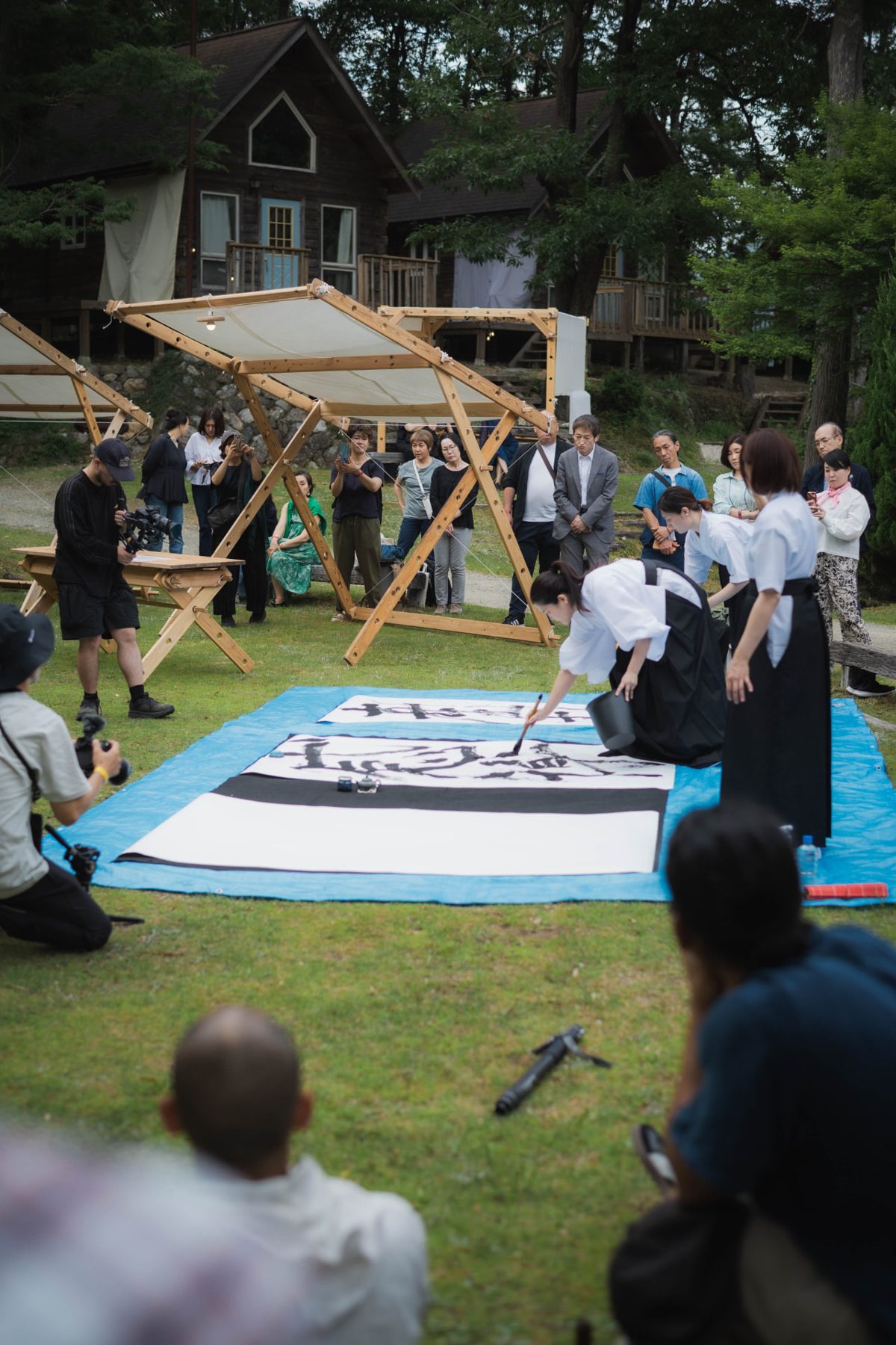 Two artists performing large-scale calligraphy on paper as a crowd watches