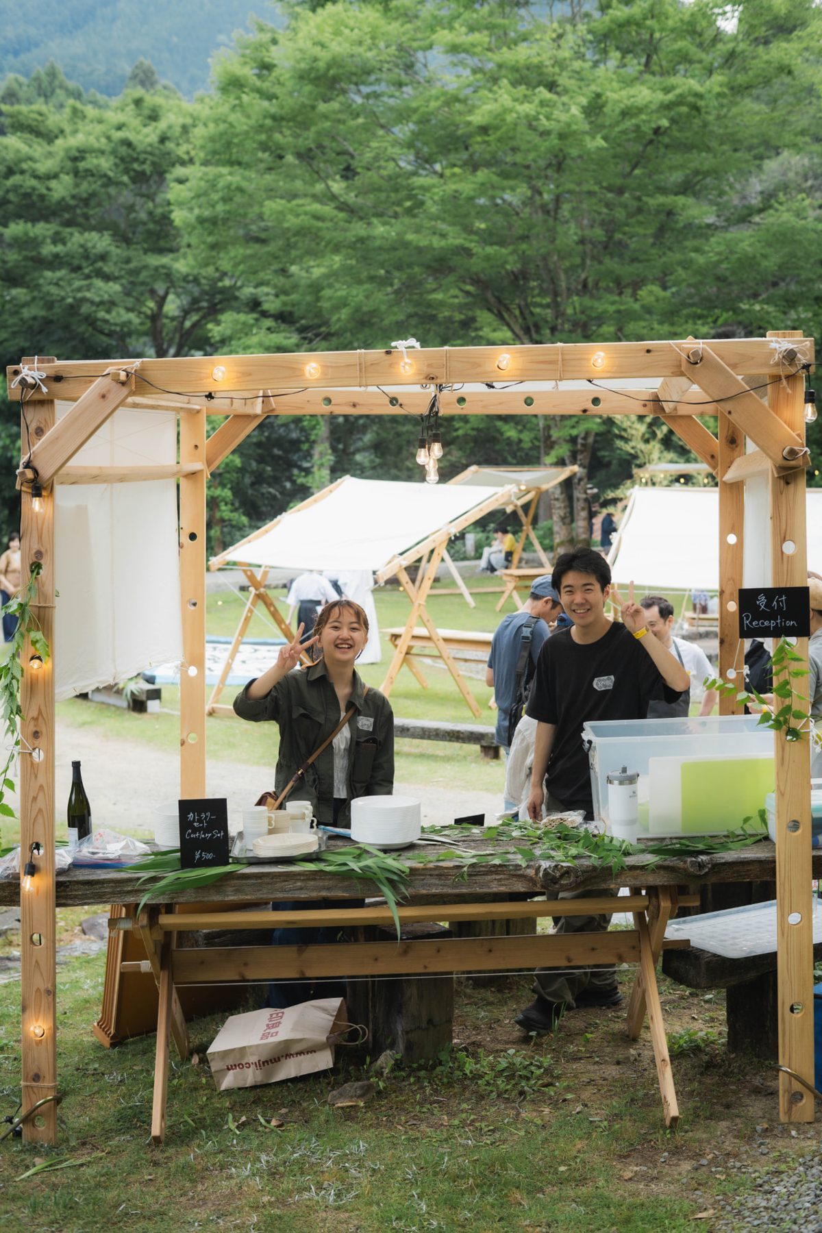 Two hosts smiling behind the wooden reception stand in the forest