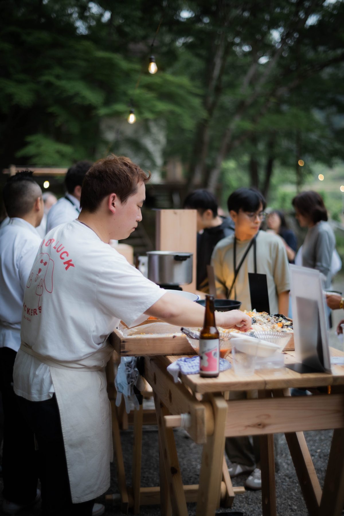 A chef plating a large platter at a wooden stand under evening string lights