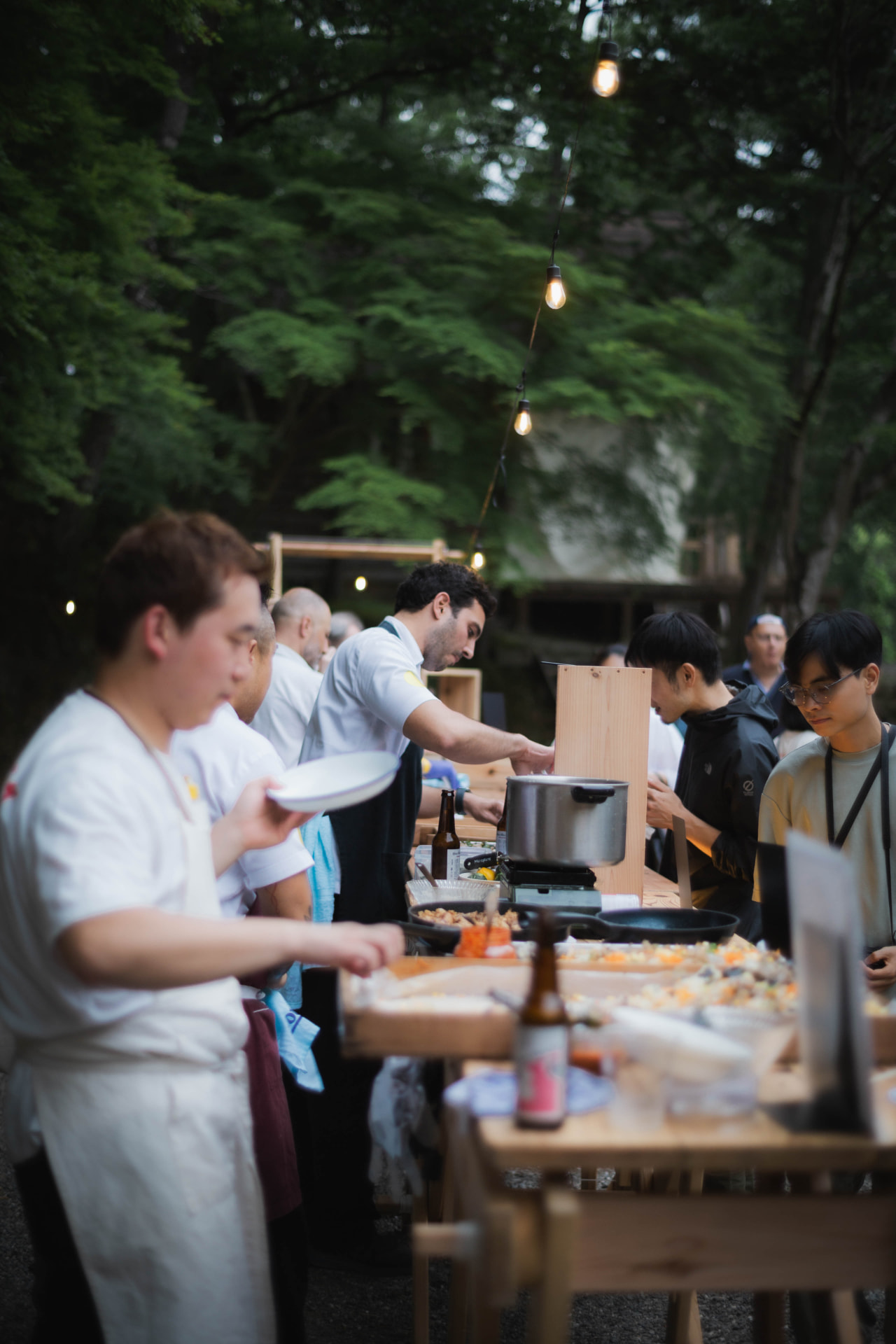 Chefs cooking side by side along a long wooden serving table at the festival