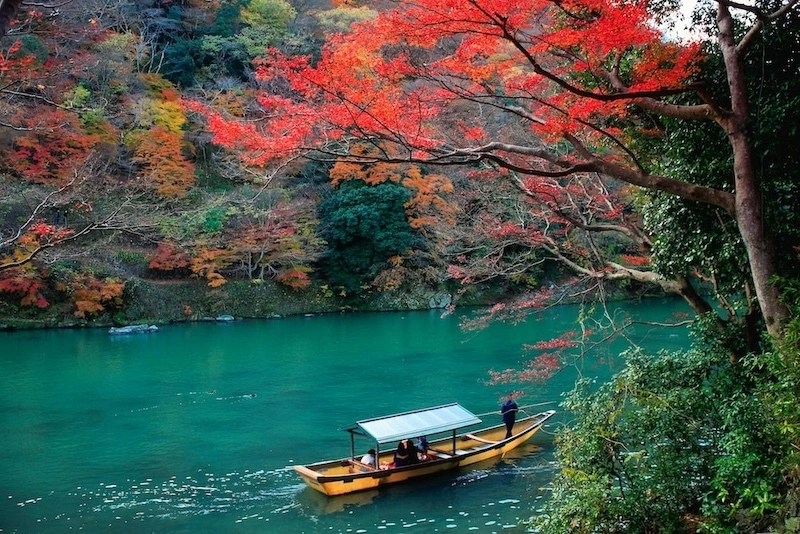 A traditional boat drifting down the Hozugawa river through autumn maples near Kameoka