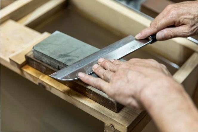 Hands sharpening a Japanese kitchen knife on a whetstone