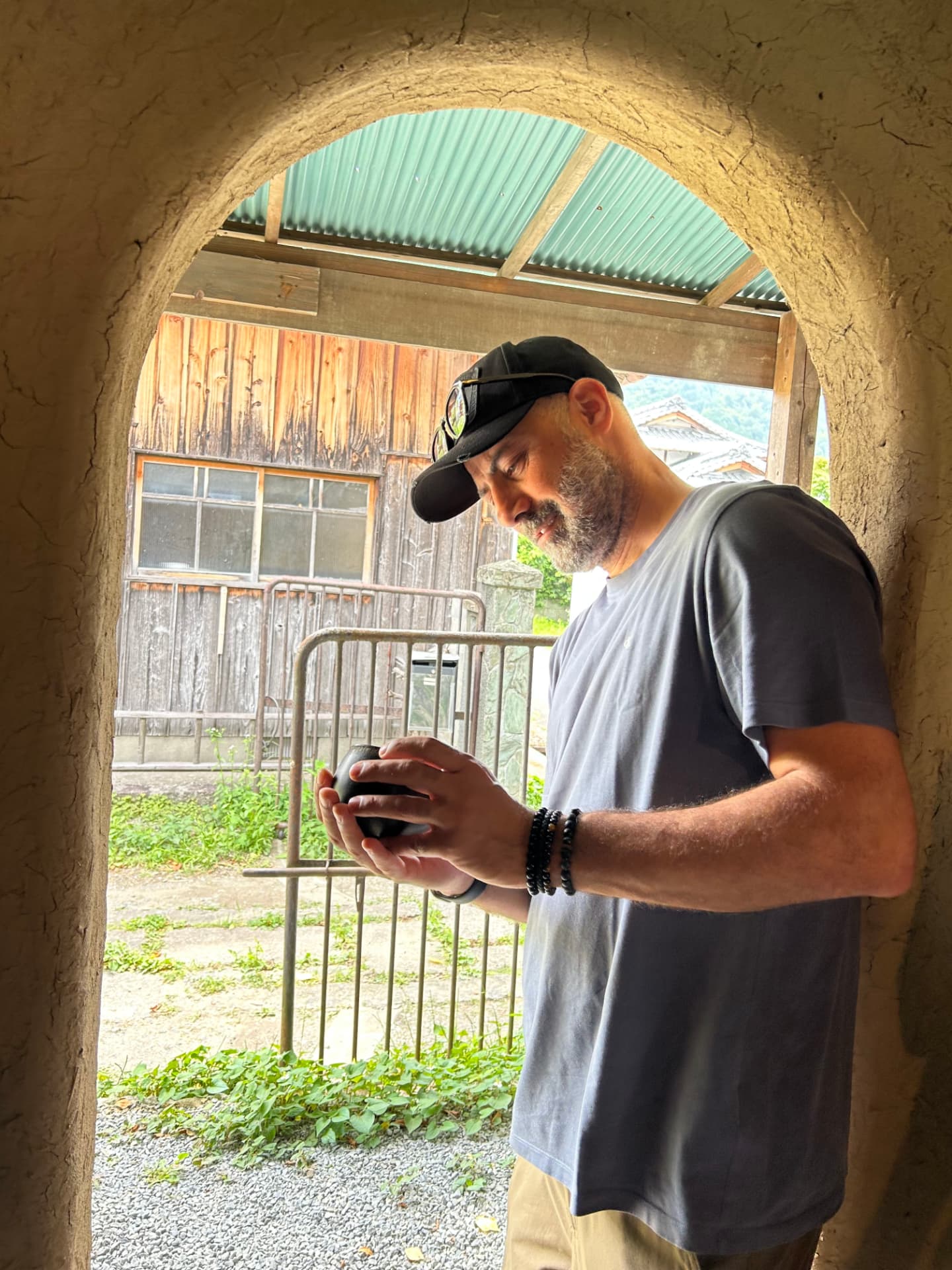 A chef examining a hand-thrown black ceramic vessel in an earthen doorway